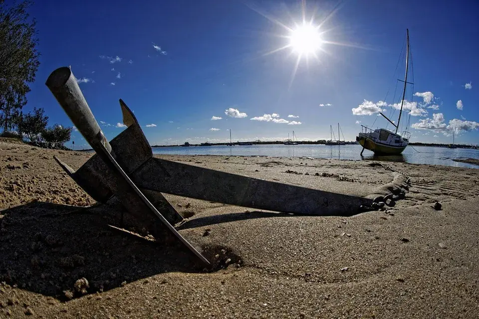 Sailboat anchored near a beach with the anchor line visible in the foreground